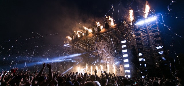 a stage with lights and streamers, behind an excited crowd with their arms in the air.