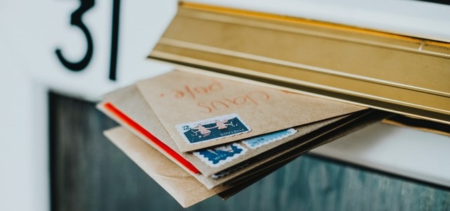 brown paper envelopes with stamps hanging outside of a mailbox.