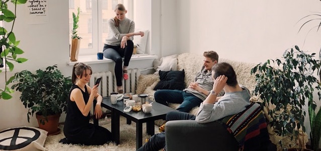 a group of friends sitting in a living room chatting and laughing together.