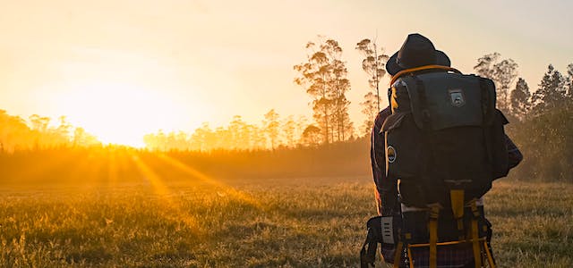 man hiking through a field at sunset with a backpack on.