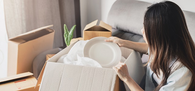 Young happy woman moving in new home and unpacking cardboard boxes