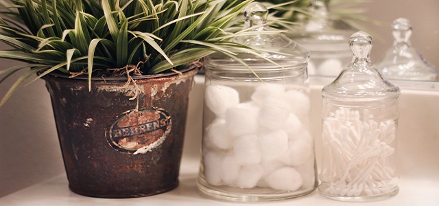 cotton swabs in a glass jar next to a leafy green plant.