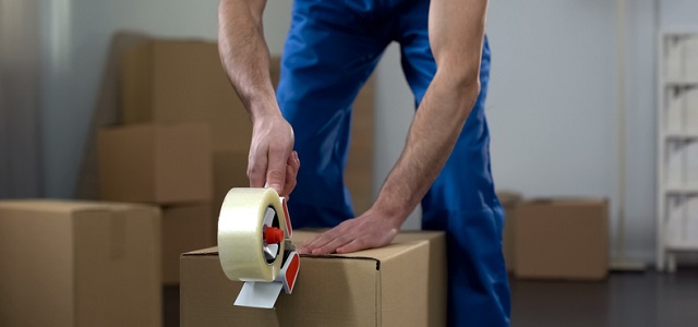Moving company worker packing cardboard boxes, quality delivery services