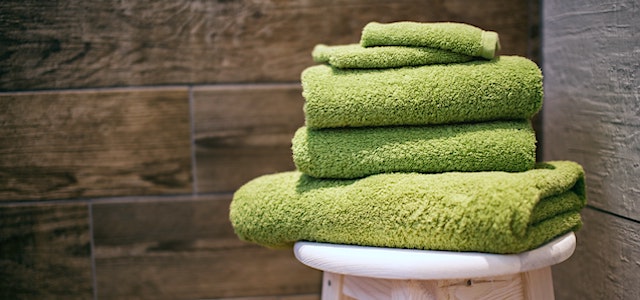 green folded towels sitting on a stool in a tiled bathroom.