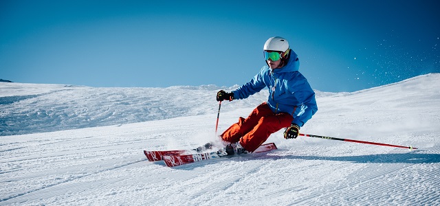 a skier gliding down a ski slope with blue skies and a blue jacket.