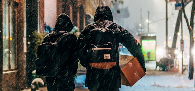 Two people carrying boxes down a snowy street in preparation for an apartment move.