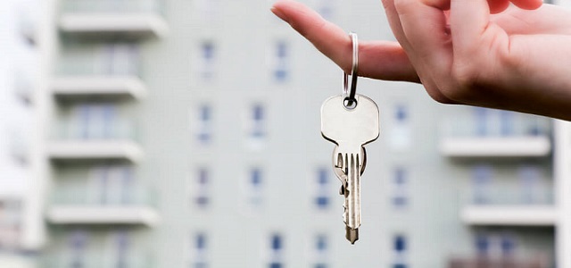 A hand holding a key in front of an apartment building.
