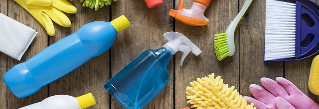 Colorful cleaning bottles and supplies on a light wooden floor.